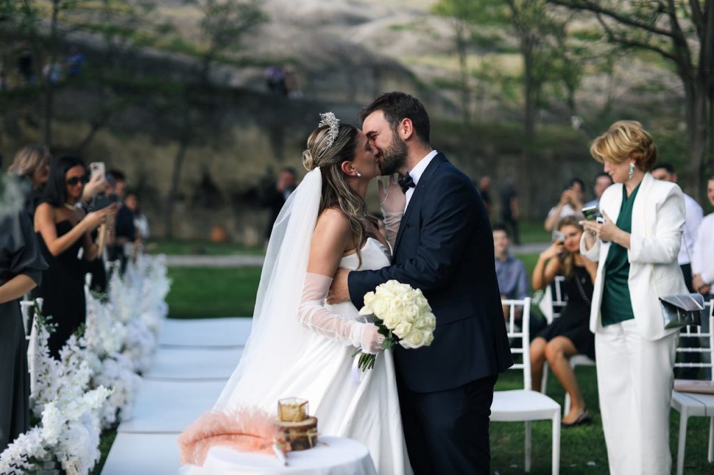 A newlywed couple shares a romantic kiss during an outdoor wedding ceremony.